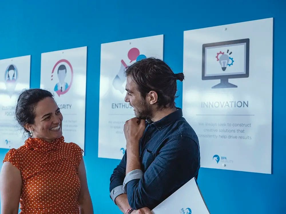 Male and female colleague stood in front of a wall of posters, having a chat