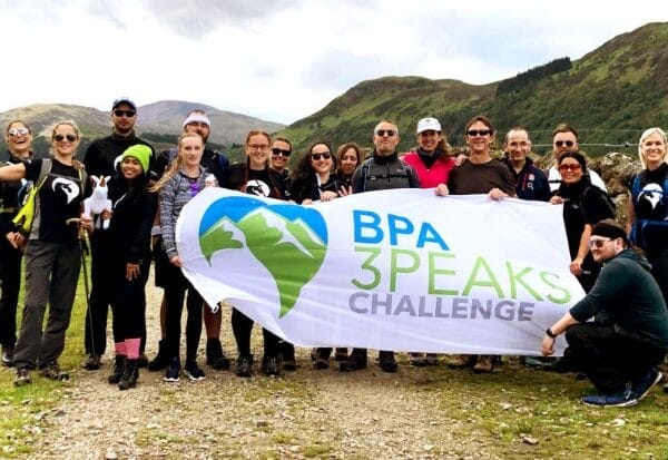 Group of BPA Quality employees stood in front of hills with a 3 peaks challenge flag